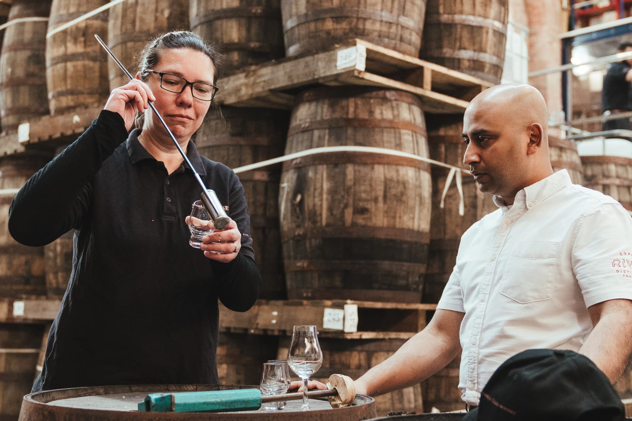 Copper Rivet distillery staff sampling spirits among oak barrels, showcasing the brand’s craft heritage and team-led hospitality experience.