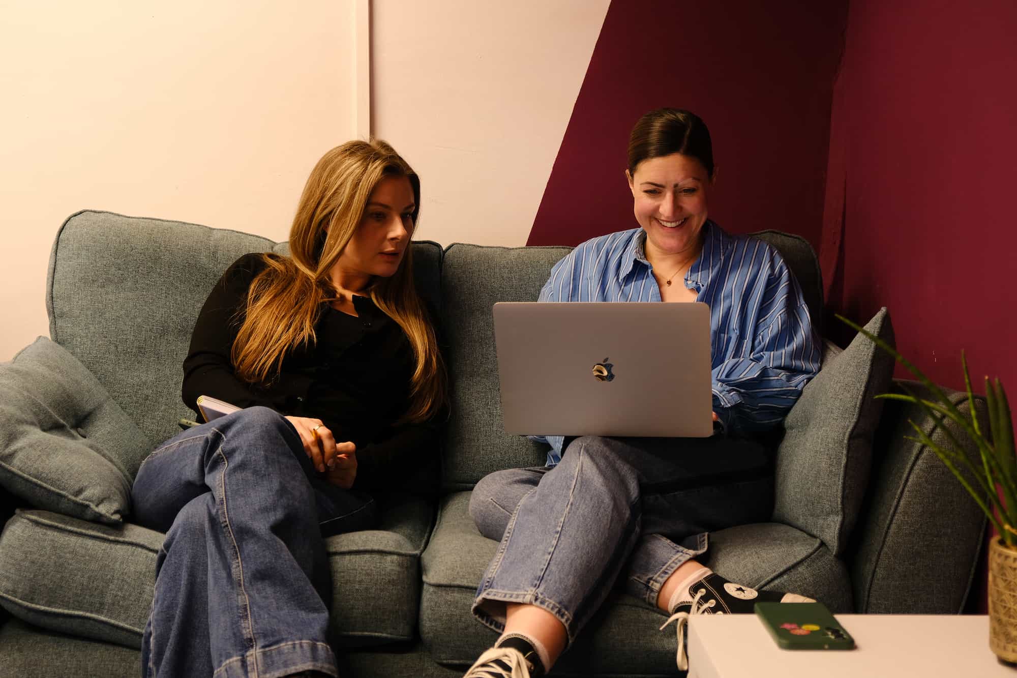 Two colleagues named Laura sitting on a sofa working together on a laptop.