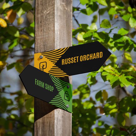 Chegworth Valley orchard signage with branded direction signs pointing to Russet Orchard and farm shop in English apple orchard.